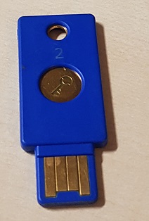 Blue Yubikey with golden button and pins on a brown desk